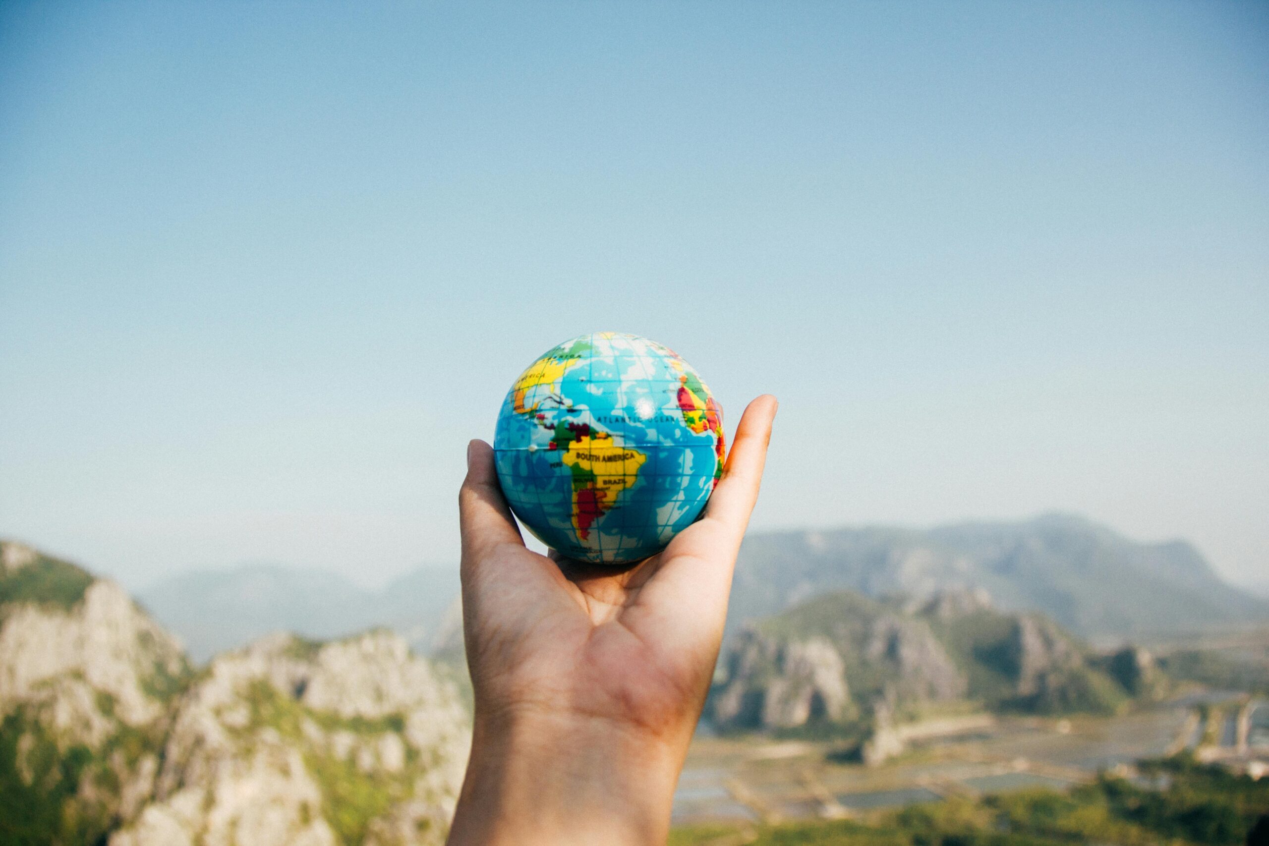 About 1 Hand holding a globe against a mountain background symbolizing travel and exploration.